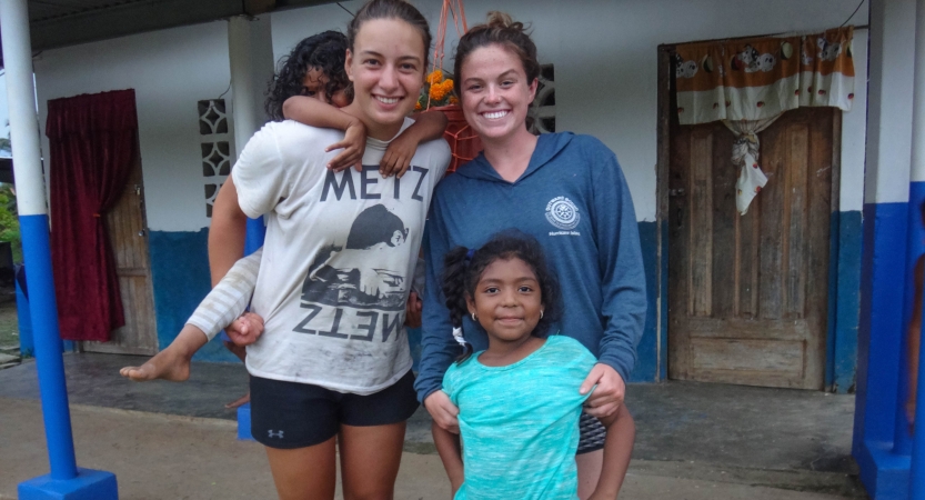Two Outward Bound students pose for a photo with two small children during a service project.